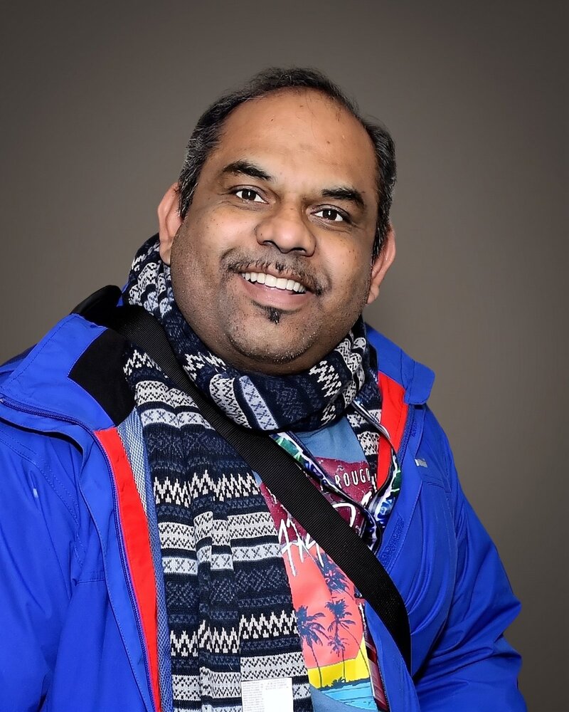 Dr Menon smiling, wearing a blue jacket and patterned scarf