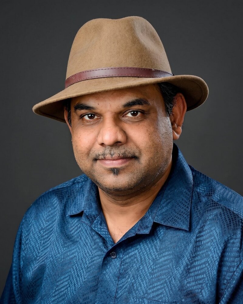 Dr Menon in a fedora and teal shirt